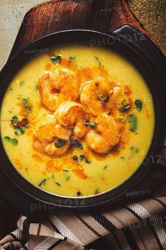 Creamy shrimp curry with spices, garnished with herbs, on a textured background, homemade, no people