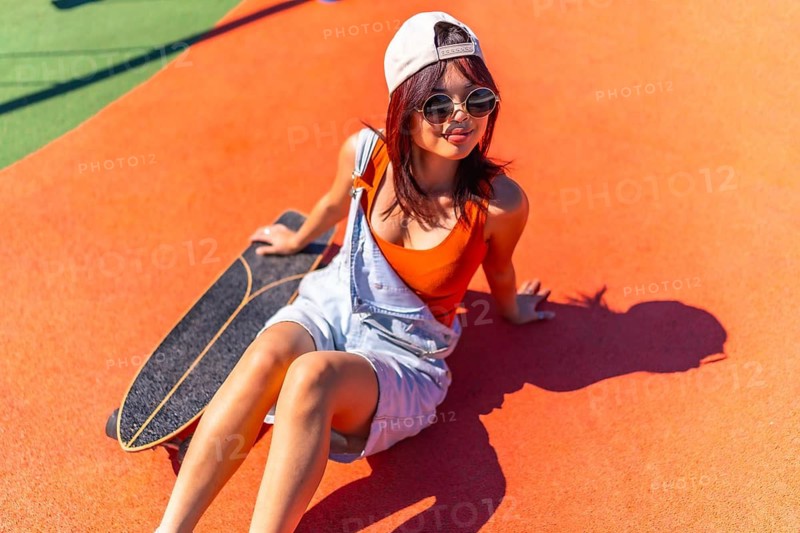 Top view of a cool chinese woman sitting next to skateboard in a colorful urban park