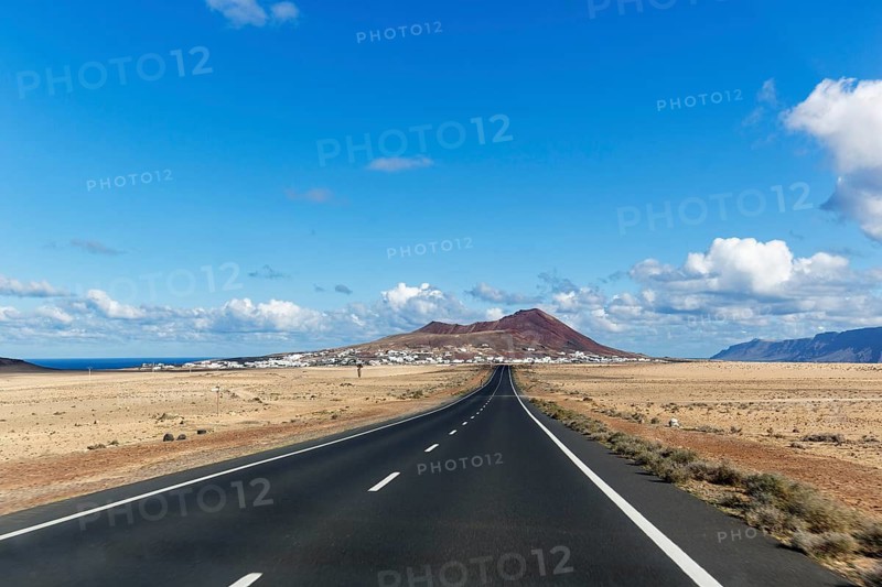 Empty straight country road and Soo village, Caldera Trasera on the horizon, El Jable, Lanzarote, Canary Islands, Spain