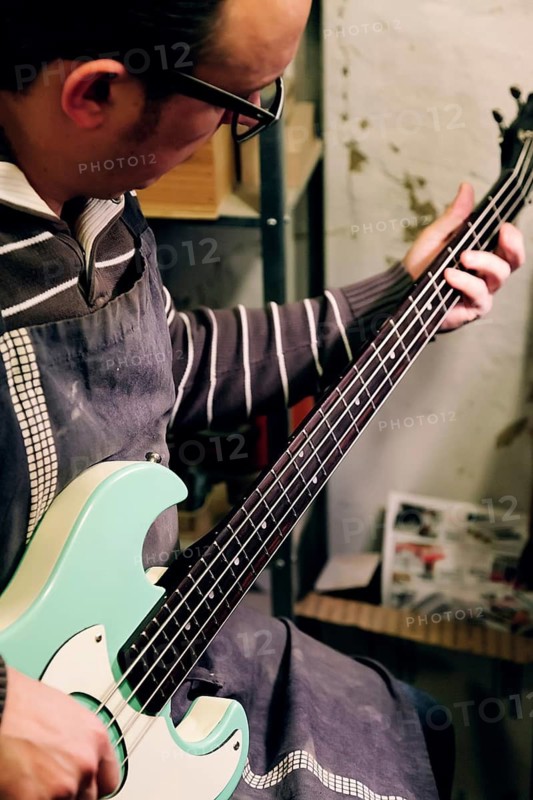 A skilled luthier works meticulously on a bass guitar in a workshop, showcasing the art of instrument craftsmanship. The workspace is filled with tools and materials
