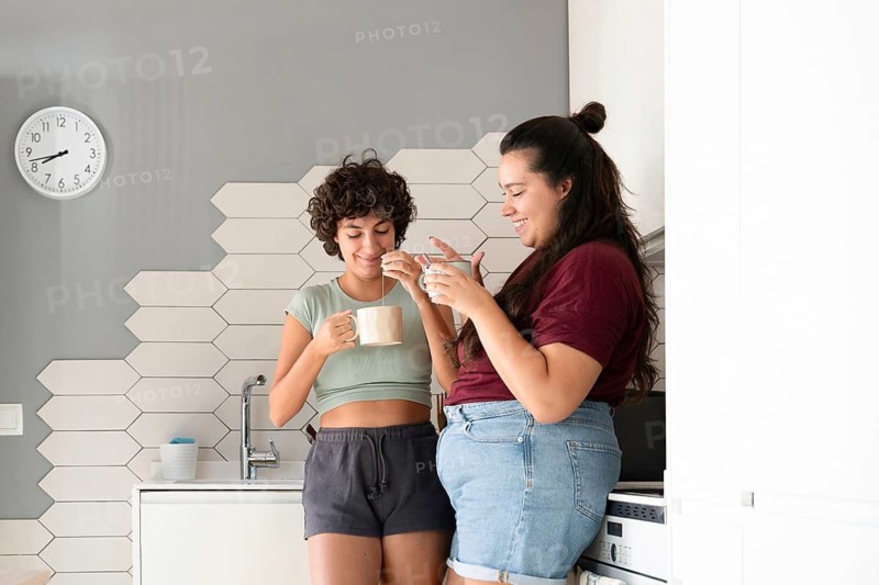 A loving lesbian couple enjoys a morning coffee together in their modern kitchen. They share smiles and warmth, creating a cozy and intimate atmosphere