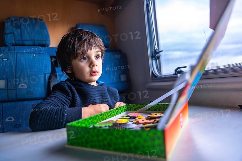 Young boy concentrating on completing a puzzle while sitting at a table inside a camper van, parked at fangar beach in tarragona's ebro delta