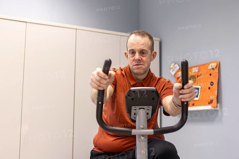 A man participates in a wellness activity on an exercise bike in a mental health day center, focusing on physical health and well-being