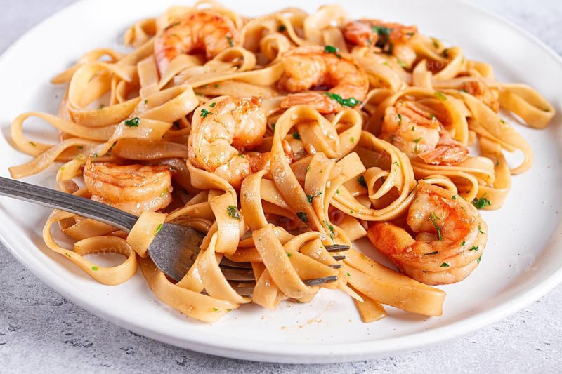 Fettuccine pasta with shrimp, spicy in soy sauce, on a grey plate with a fork, close-up