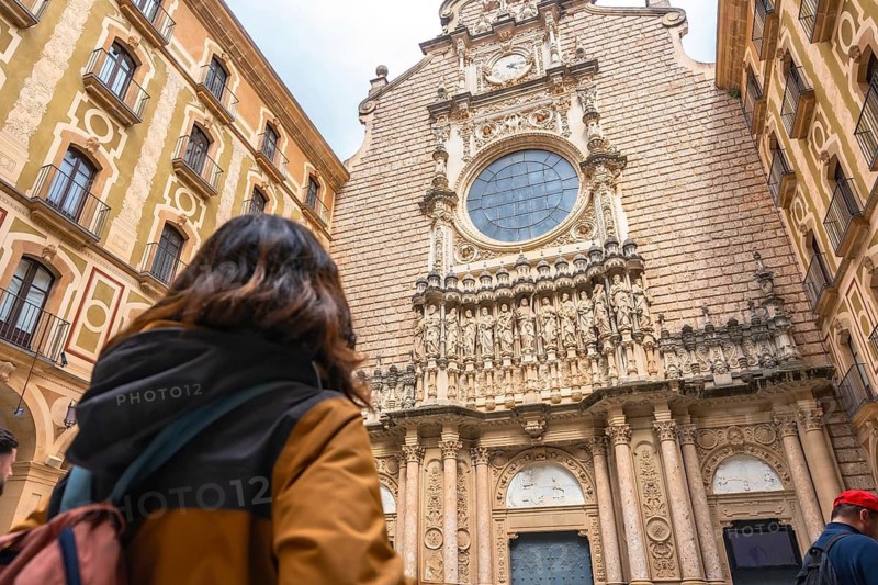 Tourist admiring the architecture of santa maria de montserrat abbey, a benedictine monastery located on the mountain of montserrat, in monistrol de montserrat, catalonia, spain