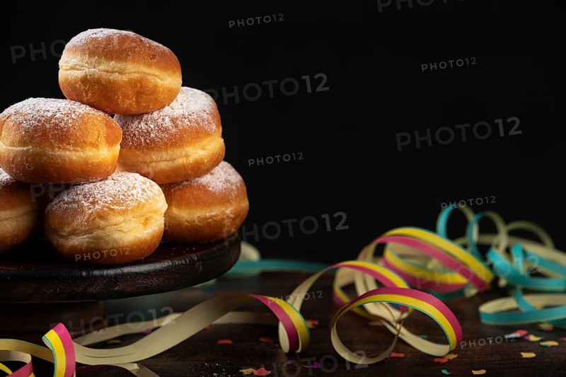 Pile of doughnuts with colourful paper streamers and confetti on a dark table, carnival