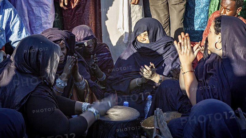 Women concentrate on drumming and prayer, in black and purple clothing, Traditional woman make music at the Tuareg Festival of Tamanrasset in the Sahara in Algeria