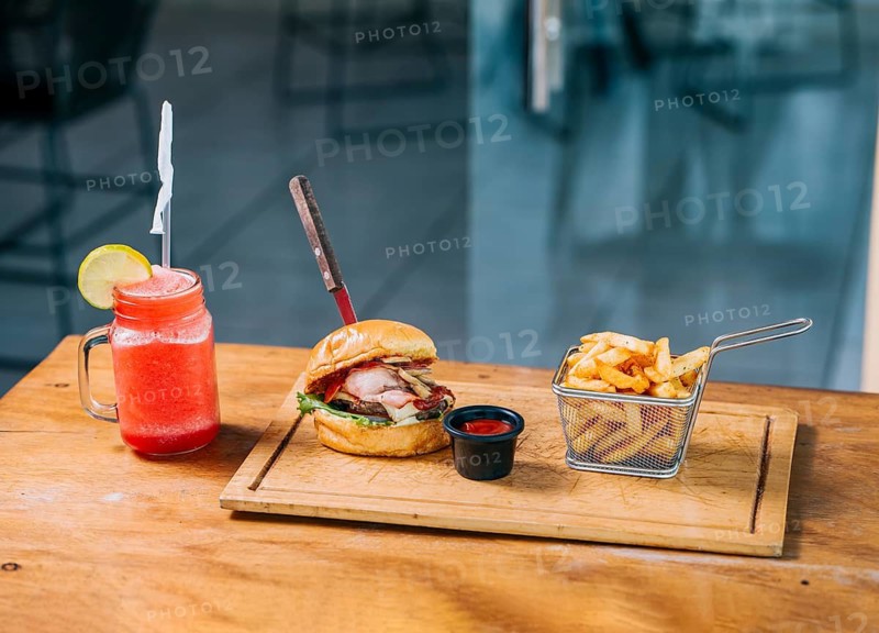 Big beef burger with fries and refreshing drink served on wooden table
