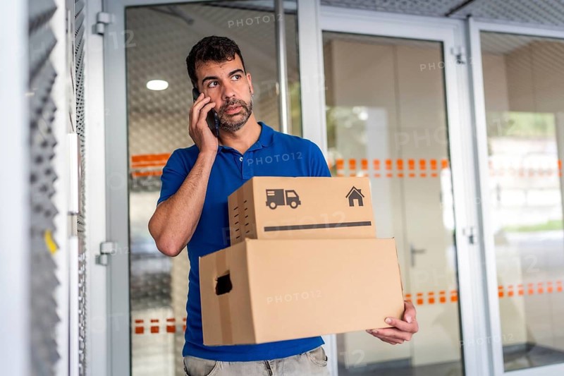 Delivery man talking to the mobile in front of a door of a house