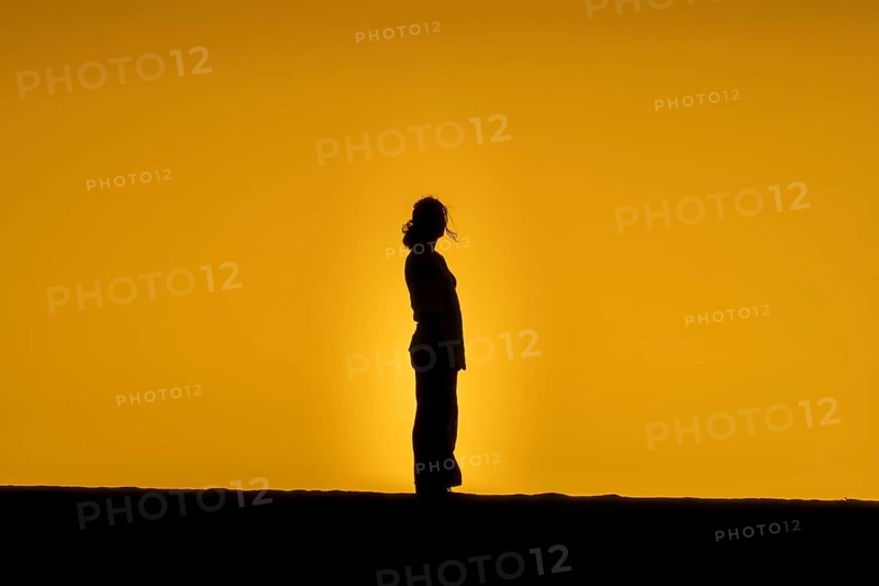 A woman's silhouette is silhouetted against a golden sunset on the sand dunes of Fuerteventura, capturing a moment of solitude and beauty. Warm tones create a peaceful and inspiring scene