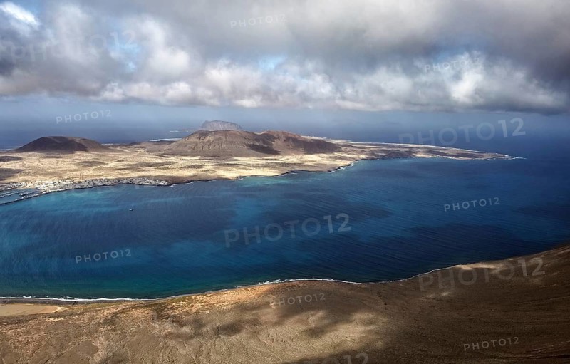 Wide island view La Graciosa with clouds in the sky over the deep blue sea and the coastline, Lanzarote, Canary Islands, Spain