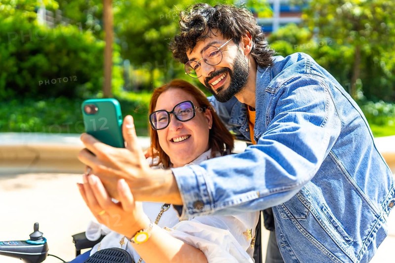 Smiling friends enjoying a sunny day outdoors, capturing a joyful selfie while celebrating inclusion, mobility, and friendship in the park