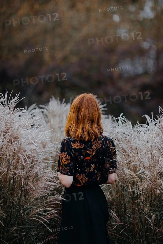 A woman with red hair stands among tall grasses in Quebec, Canada, embodying the serene beauty of autumn. The scene captures the essence of tranquility and nature's splendor