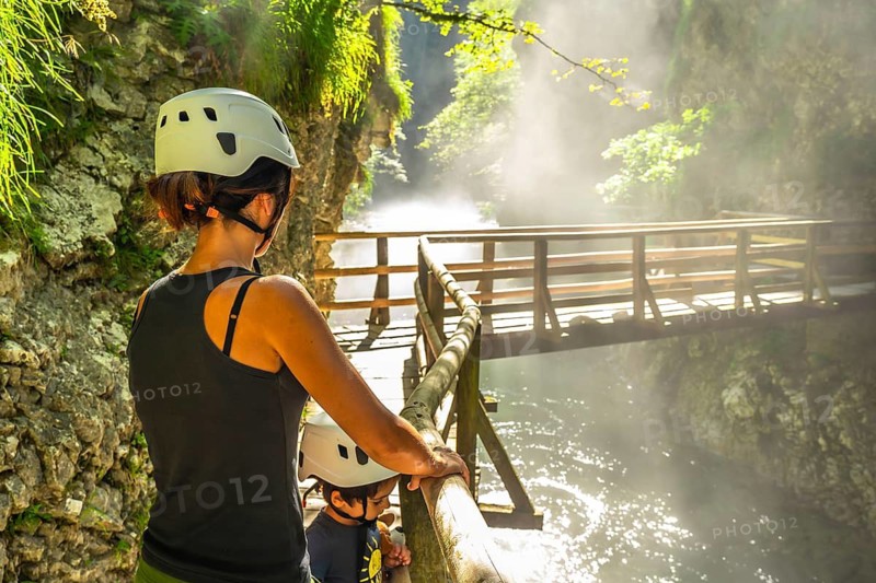 Mother and child wearing helmets, enjoying breathtaking view of wooden bridge over radovna river in vintgar gorge near bled, slovenia