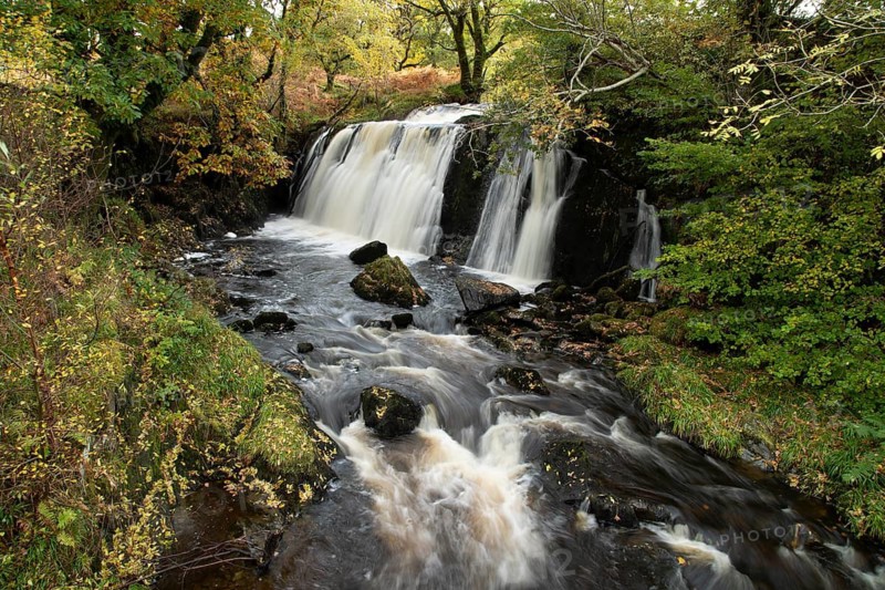 Waterfall in a woodland with autumn colour leaves in the landscape, Scotland, United Kingdom