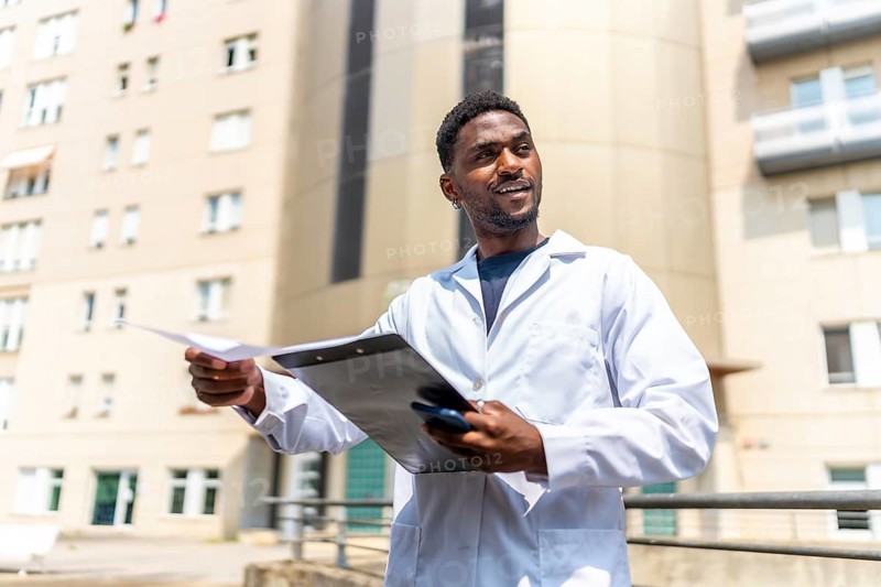 Confident African doctor with white lab coat working holding medical records outside the hospital