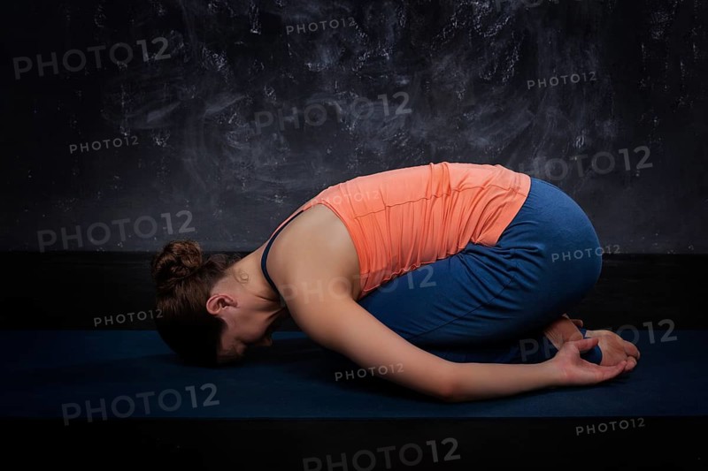 Beautiful sporty fit yogini woman practices yoga asana balasana (child's pose), resting pose or counter asana for many asanas on dark background