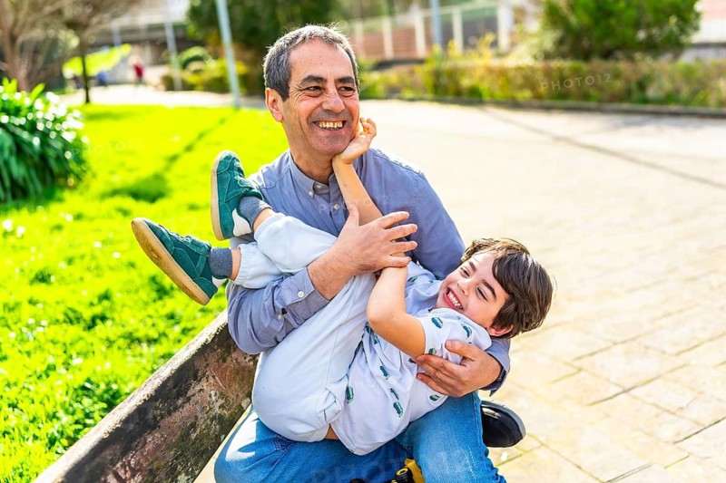Grandfather and grandson are enjoying a playful moment together in a park, laughing and bonding on a sunny day