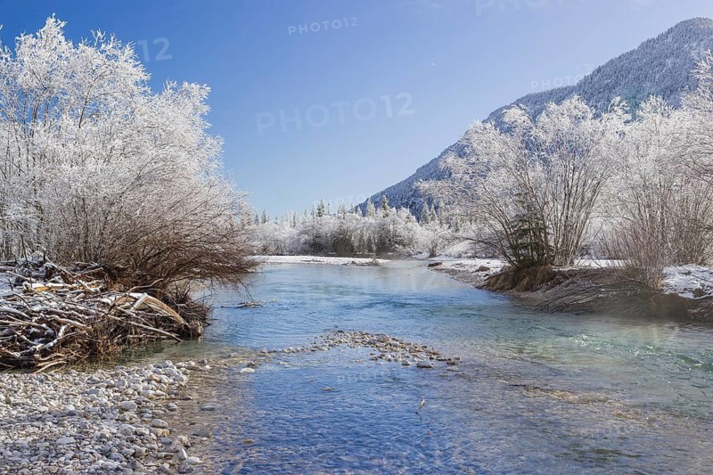 Isar valley in winter at temperatures of minus 18 degrees Celsius. Snow covered landscape with the Isar river flowing through. Some hoar frosted trees. Early morning
