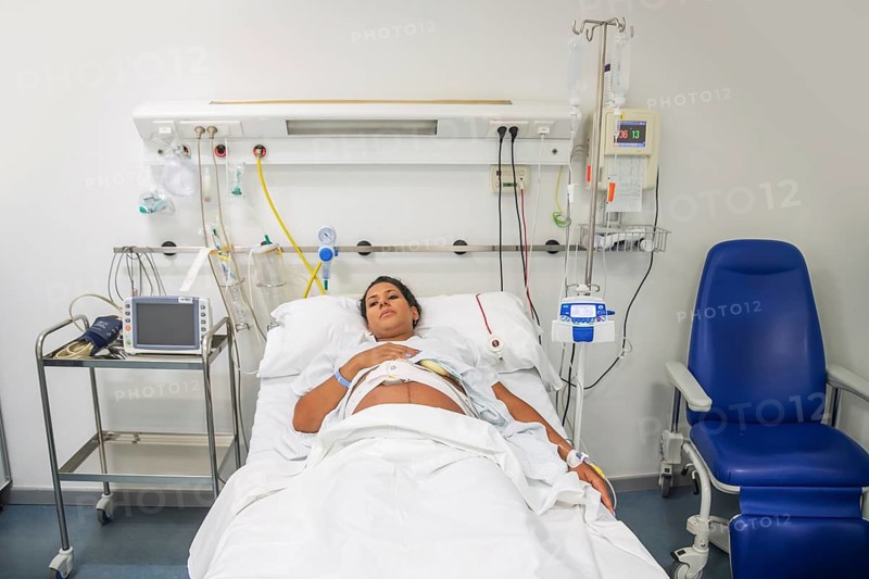 A new mother in a hospital bed, ready to give birth. Surrounded by medical equipment, she rests calmly, anticipating the arrival of her baby with a sense of love and care