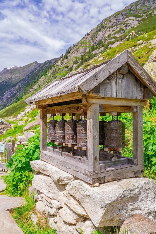 Traditional wooden prayer wheels stand on a stone foundation in the midst of an impressive mountain landscape, Little Tibet, Zillertal, Austria