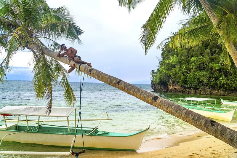 Young man relaxing on a palm tree over a tropical beach in kangbangyo island, siargao, philippines