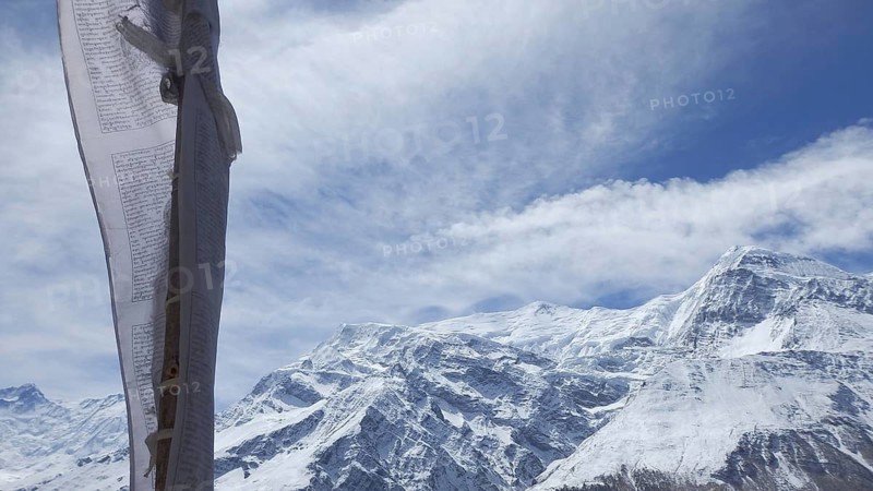 Close-up of a prayer flag in the foreground in front of majestic snow-capped mountain peaks, trekking at Annapurna Circuit, Manang, Nepal