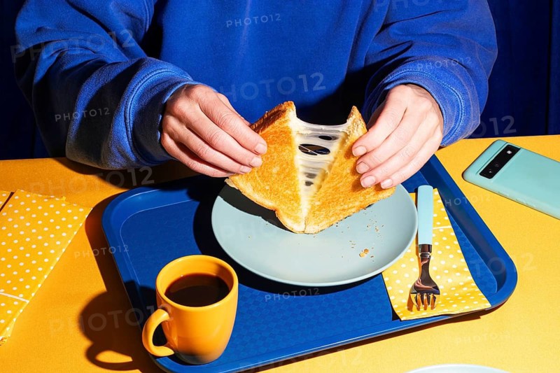 From above, a close-up shot of hands pulling apart a grilled cheese sandwich, revealing melted cheese