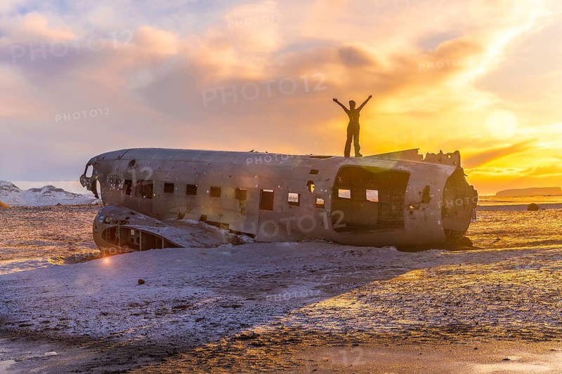 Woman on her back with her arms up on top of the Solheimasandur plane at a winter sunrise in Iceland