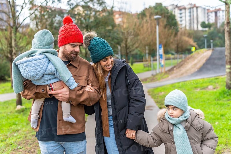 Smiling parents holding their children's hands, enjoying a leisurely stroll through a park on a chilly winter day