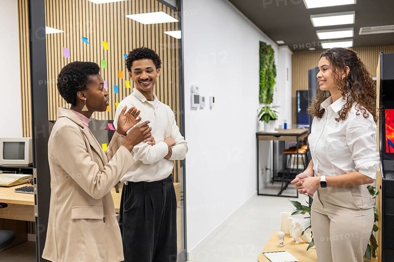 Three colleagues engage in a lively discussion in a stylish office environment with colorful sticky notes and greenery, promoting creativity and collaboration