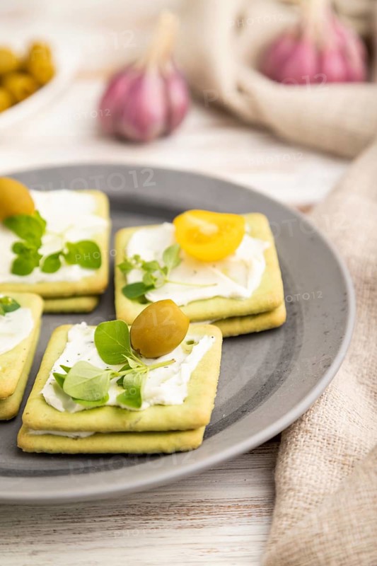Green cracker sandwiches with cream cheese and cherry tomatoes on white wooden background and linen textile. side view, close up, selective focus