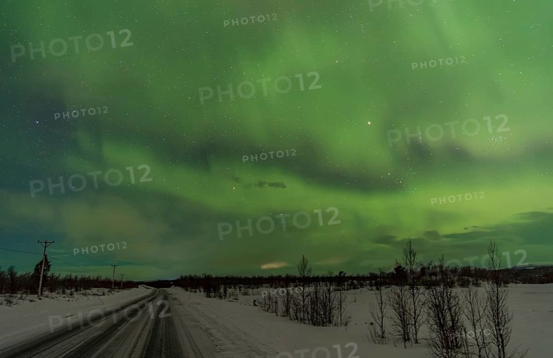 Stunning view of the Aurora Borealis illuminating the night sky with vibrant green hues above a snow-covered road and landscape near Kiruna, Sweden