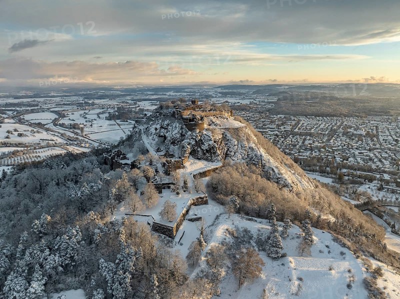 Aerial view of the snow-covered Hegau volcano Hohentwiel with Germany's largest castle ruins on a cold winter morning, at sunrise, on the right the town of Singen, district of Constance, Baden-Württemberg, Germany