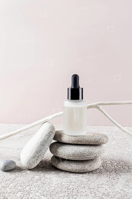 A minimalist skincare bottle with a black dropper cap rests on stacked stones against a neutral background This image embodies tranquility and simplicity in beauty care