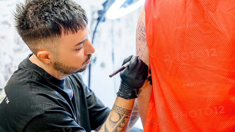 A tattoo artist skillfully inks a detailed dog tattoo on a person's arm, showcasing his concentration and expertise in a vibrant studio environment, surrounded by tools and art
