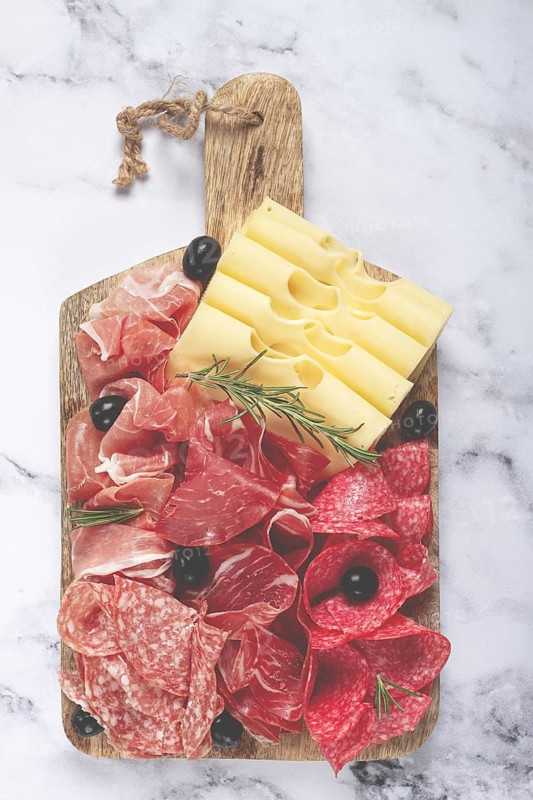 Assorted meat, appetizer, prosciutto, salami and ham, with maasdam cheese and olives, on a wooden board, breakfast, top view, close-up, no people