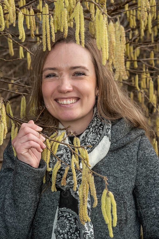 Happy young Caucasian woman without allergy problem standing by flowering hazel bush in Ystad, Skåne County, Sweden, Scandinavia