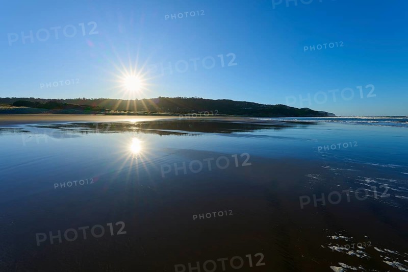 Early morning sun rays reflecting on the calm sea surface on a clear beach, Muriwai Beach, Auckland, North Island, New Zealand