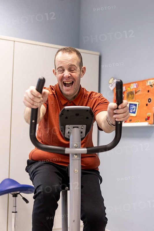 A joyful individual using an exercise bike at a day center designed for people with disabilities. The image highlights happiness, fitness, and inclusivity in a supportive environment