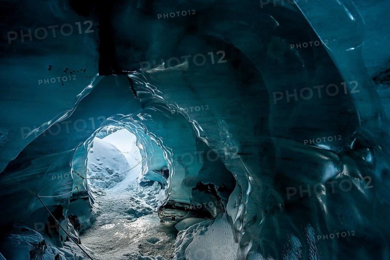 A mesmerizing view from within an ice cave at Katla Glacier, Iceland. The smooth, blue walls of the frozen tunnel open up to a snowy landscape, creating a surreal and otherworldly atmosphere