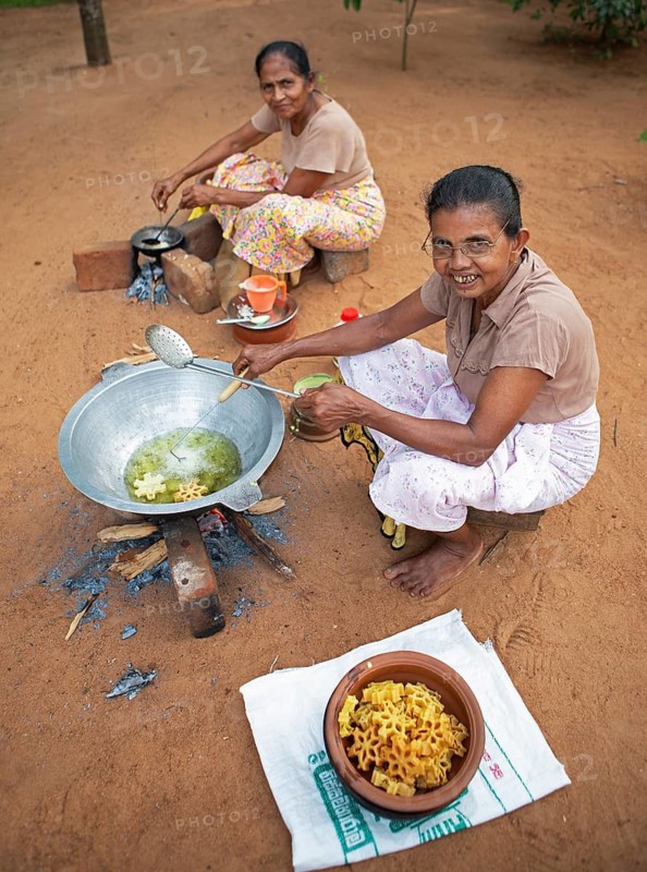 Sri Lankan woman, 62 and 63 years old, frying traditional doughnuts on a fire on the ground, Sella Kataragama, Kataragama, Uva Province, Sri Lanka