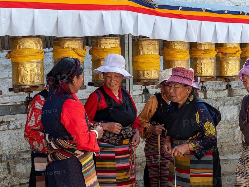 Pilgrims at golden prayer wheels, Tibetan woman in conversation, Xigaze, Tibet, China