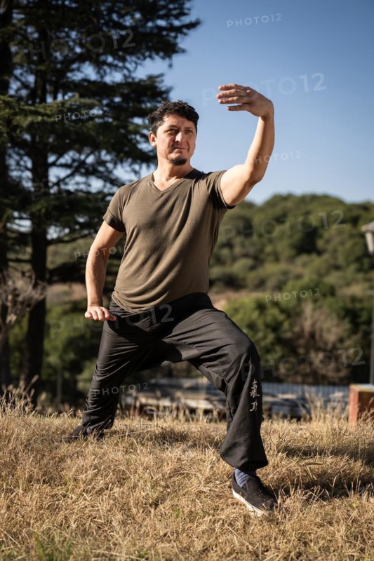 Wide shot of a man in a Tai Chi Chuan posture outdoors on a sunny day