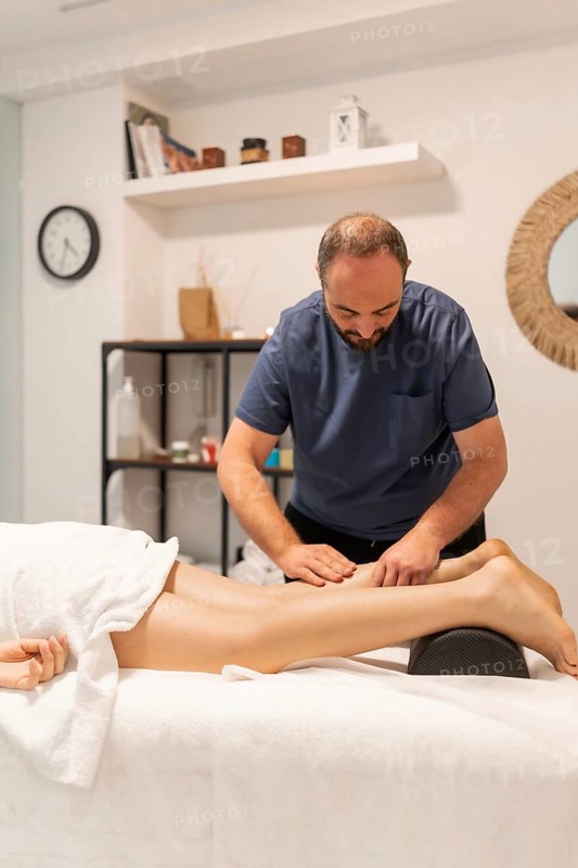 Professional masseur providing a therapeutic leg massage to a client in a spa or wellness center, focusing on relaxation, pain relief, and muscle recovery