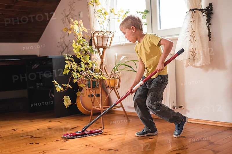 A 6-year-old boy cleaning the wooden floor with a mop
