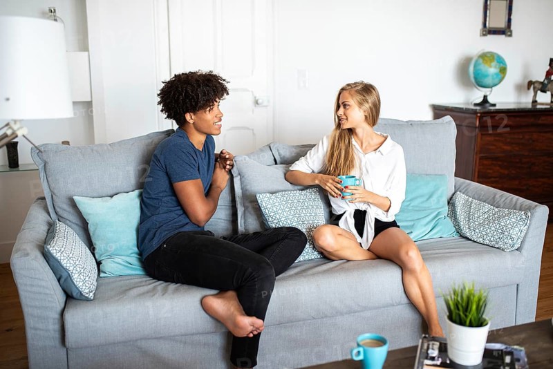 Two friends enjoy a relaxed conversation while sitting on a comfortable sofa in a modern living room. They are smiling and sharing a moment over a cup of coffee
