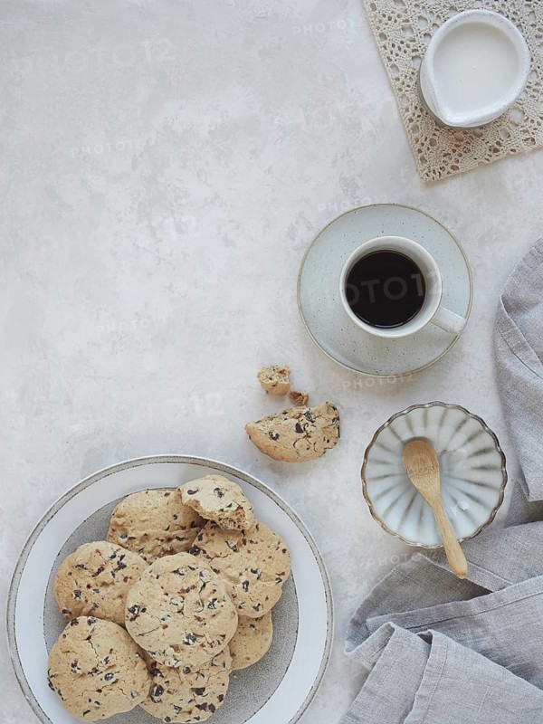 Table set for afternoon snack or breakfast with homemade cookies and coffee cup and milk jug. Top view with copy space