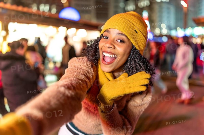 Young woman wearing yellow winter clothes taking selfie at christmas market, enjoying festive atmosphere