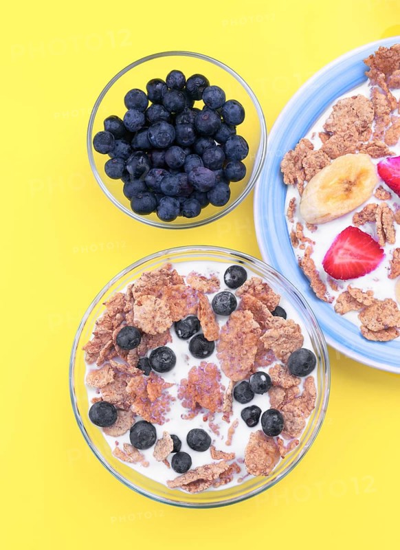 A vibrant breakfast setting featuring bowls of cereal with milk, topped with fresh blueberries, strawberries, and bananas. Complemented with a side bowl of blueberries
